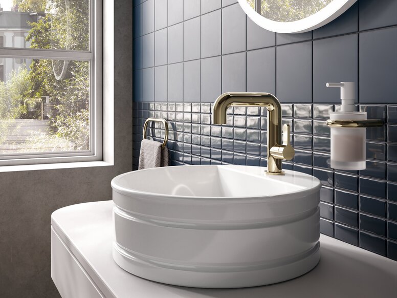 HEWI PVD AQ11 fittings A modern washbasin with a gold-coloured tap, set against dark blue tiles and a large window letting in plenty of natural light
