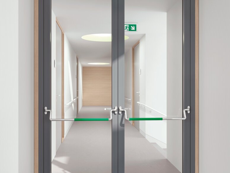HEWI panic bar Double-leaf glass door with a grey frame and panic bars with green grip surfaces in a white corridor