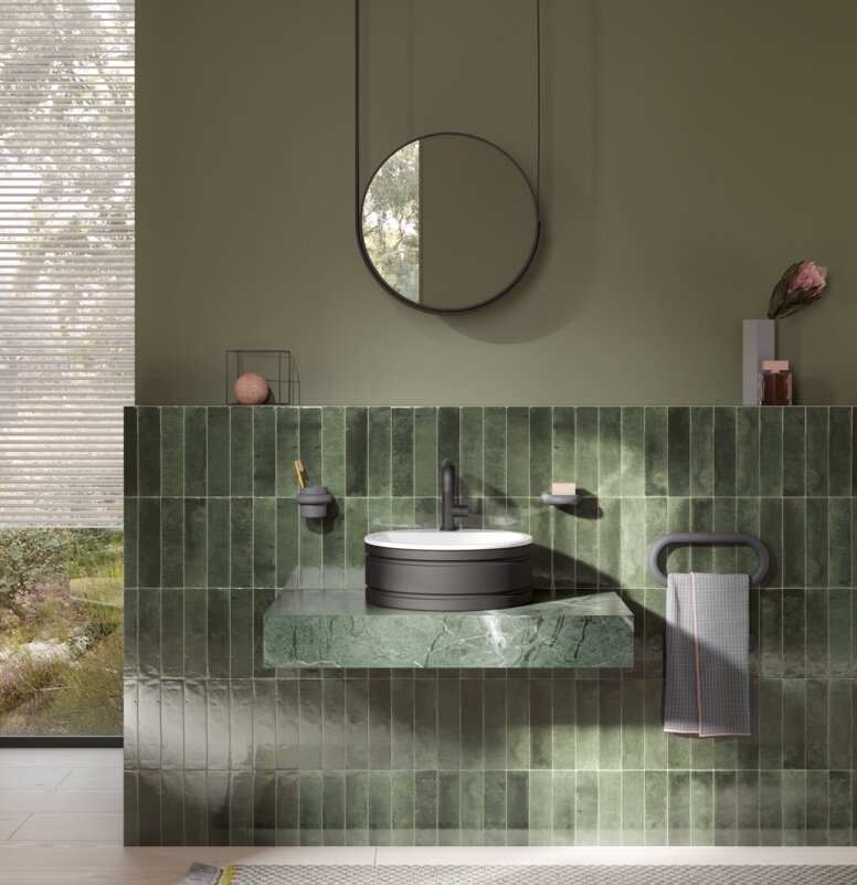 HEWI Serie 477 Interieur Rundes Waschbecken auf grünem Marmorwaschtisch mit schwarzem Wasserhahn und Handtuchhalter, darüber ein runder Spiegel