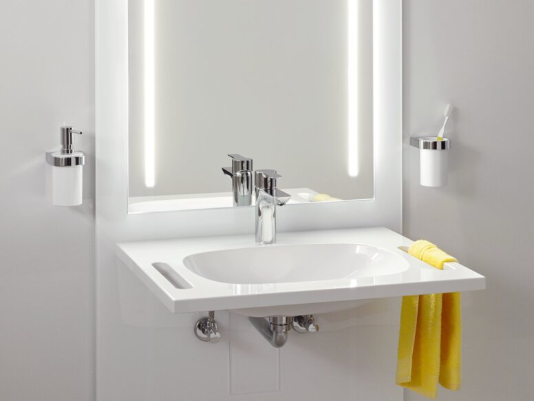 HEWI S 50 Waschtisch-Modul Weißes Waschbecken mit Wasserhahn, seitlicher Griffmulde und beleuchtetem Spiegel mit zwei Lichtleisten an hellgrauer Wand