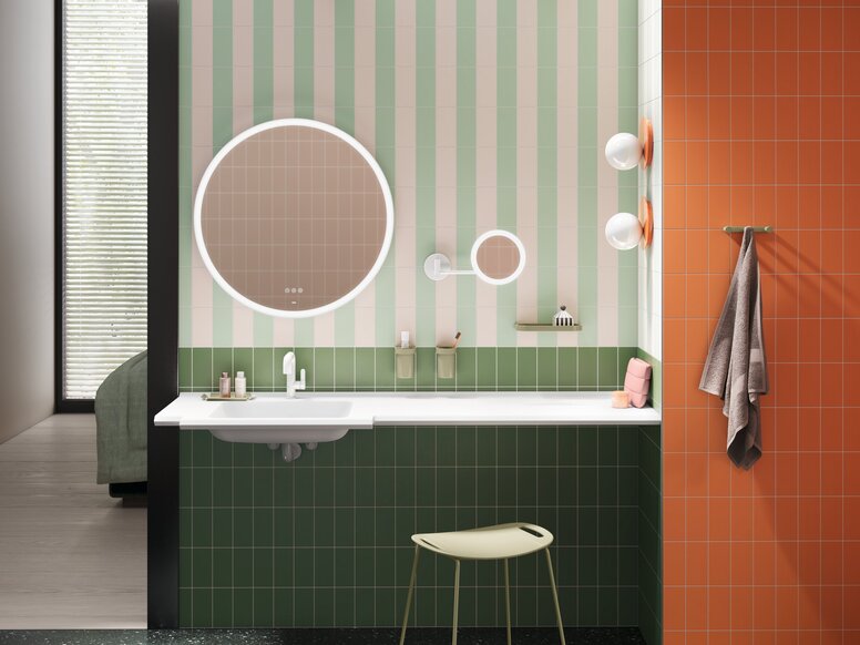 HEWI System 700 interior Washbasin with green fittings, a round mirror, cosmetic mirror and stool against a green-and-white striped wall and orange tiles