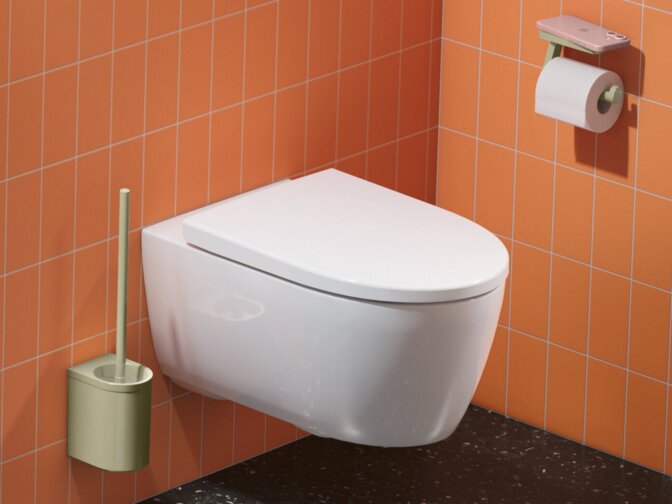 Waschtisch mit grüner Ausstattung, Rund- und Kosmetikspiegel, daneben ein wandhängendes WC mit Papierhalter vor Fliesen in Grün und Orange