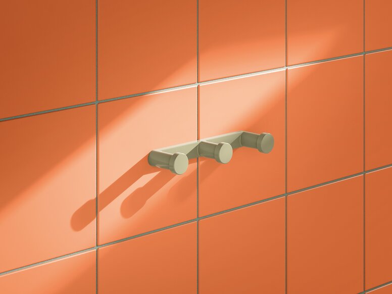 HEWI System 700 triple hook Three green plastic wall hooks with round ends mounted on a narrow strip on an orange tiled wall