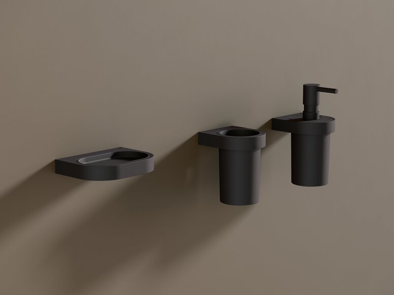 A black powder-coated soap dish, along with a tumbler and a soap dispenser, against a brown wall