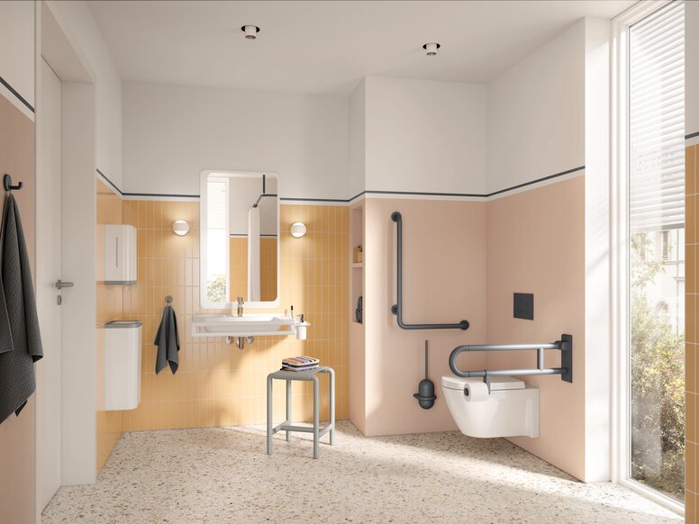 HEWI Range 801 Interior Wall-hung WC with a hinged support rail on the side and an L-shaped support rail, alongside a washbasin with a mirror and a stool