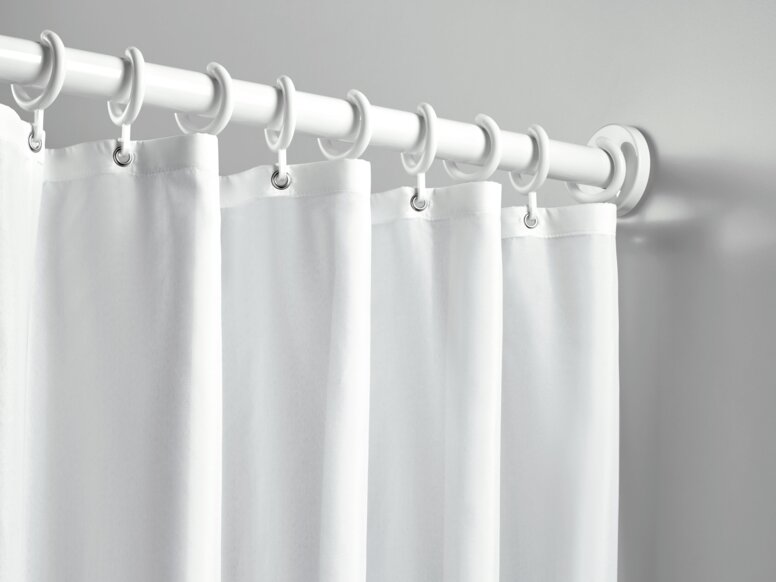 A shower curtain with white rings, hung on a white curtain rail against a light grey wall
