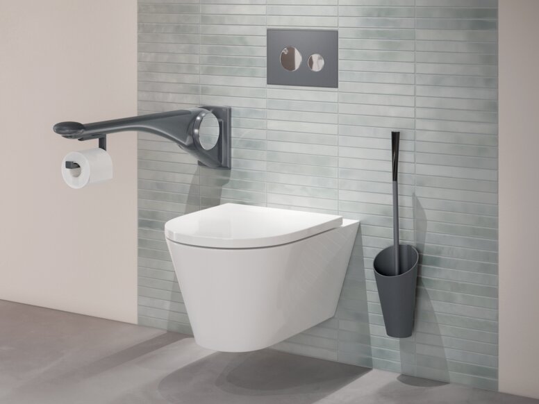HEWI Range 802 LifeSystem premium hinged support rail handle Wall-hung WC with a side support rail, an integrated toilet roll holder and a toilet brush mounted on a green tiled wall