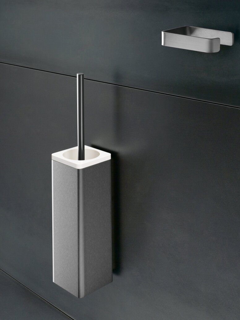 HEWI Serie 805 WC-Bürstengarnitur WC-Bürstengarnitur aus Edelstahl mit rechteckigem Behälter und Bürstengriff an einer dunkelgrauen Wand, darüber ein kleiner Wandhalter
