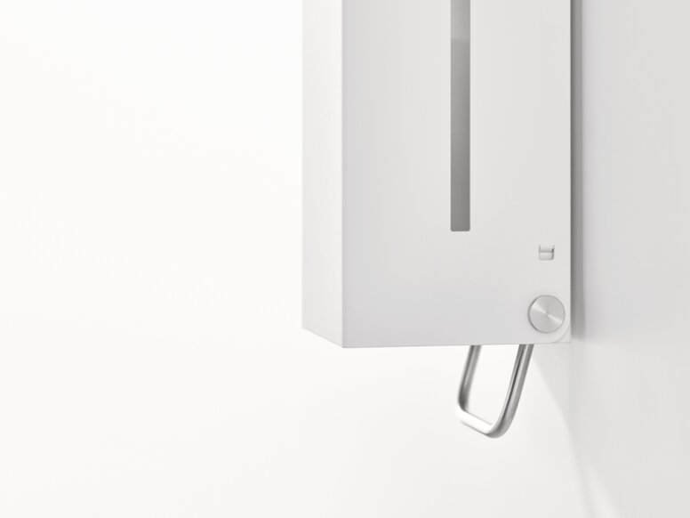 HEWI System 900 soap dispenser White wall-mounted soap dispenser with a viewing window and an operating lever on the underside against a white background