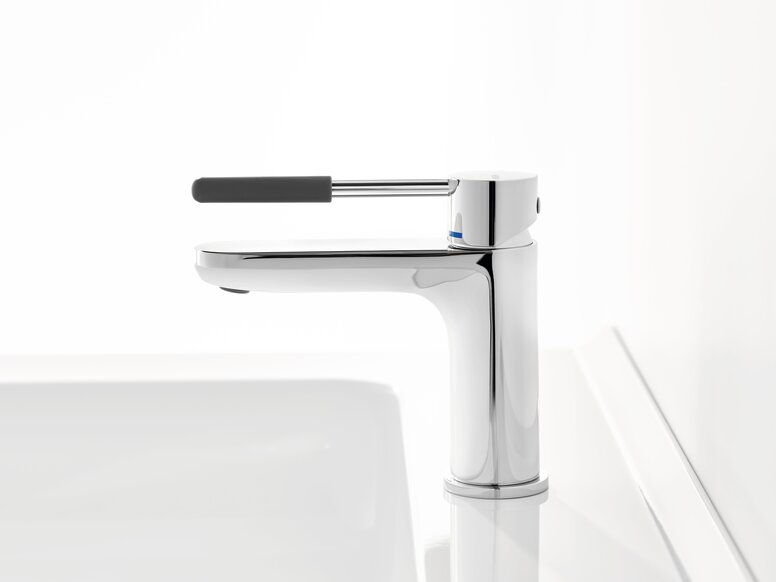HEWI AQ single-lever washbasin mixer tap Chrome-plated tap with a long lever handle and dark grey grip sleeve on a white washbasin against a white background