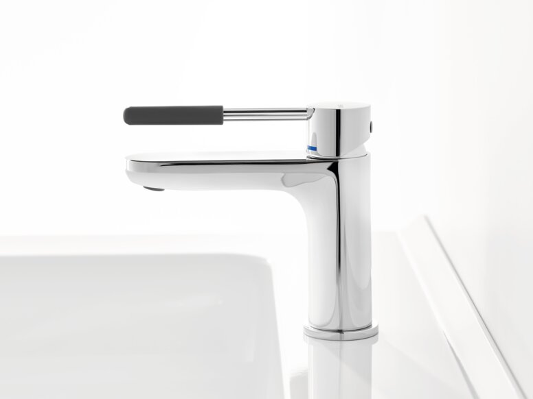 HEWI AQ single-lever washbasin mixer tap Chrome-plated tap with a long lever handle and dark grey grip sleeve on a white washbasin against a white background