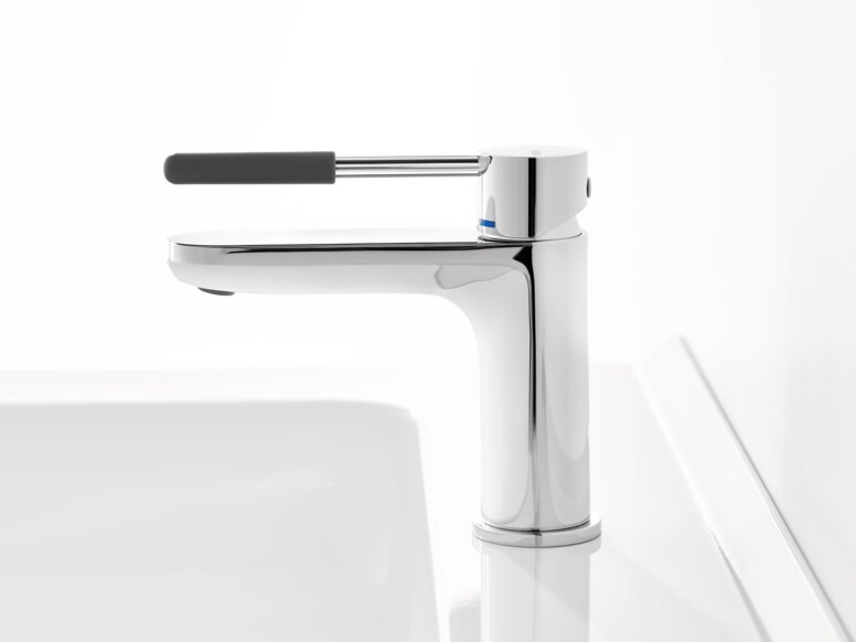 HEWI AQ single-lever washbasin mixer tap Chrome-plated tap with a long lever handle and dark grey grip sleeve on a white washbasin against a white background