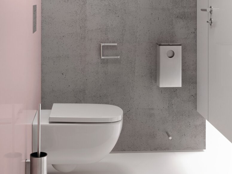 HEWI System 162 Interieur Schmaler WC-Bereich mit wandhängendem weißem WC vor einer grauen Wand in Betonoptik, weißem Toilettenpapierhalter und Toilettenbürstengarnitur sowie einer rosafarbenen Seitenwand